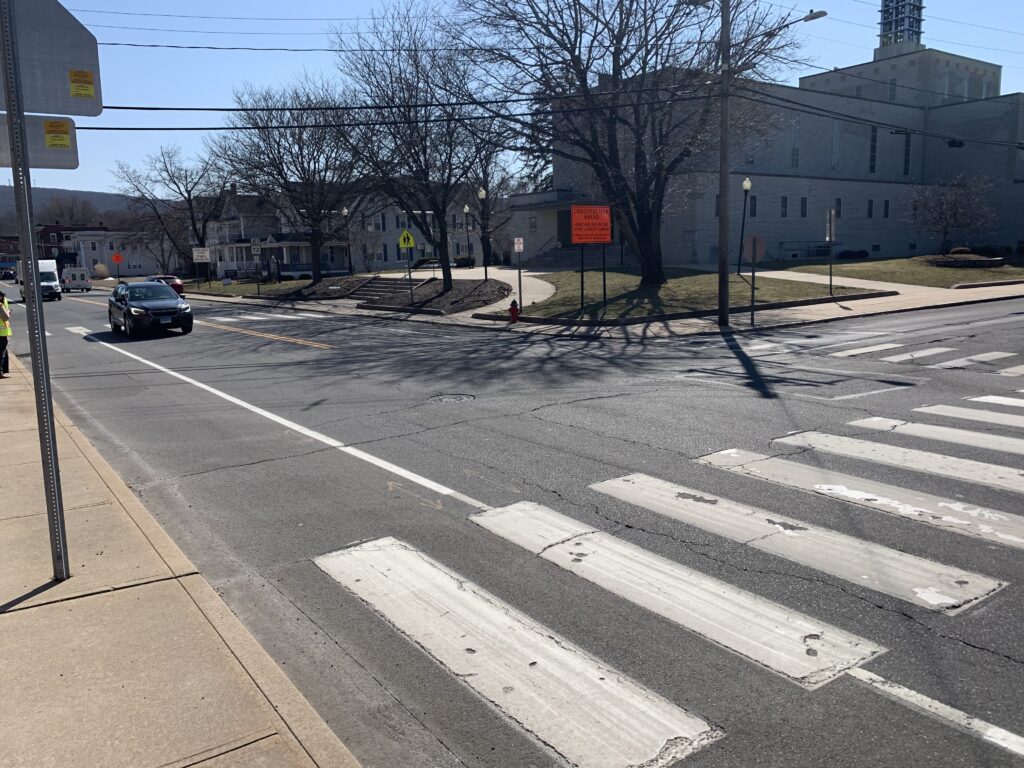 A pedestrian crosswalk appears in the foreground, with a car approaching the crosswalk. There is a church among pedestrian crossing signs in the background